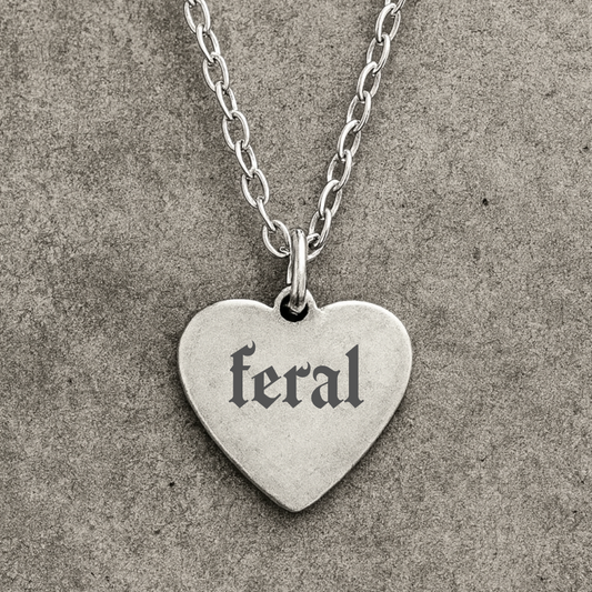 Silver heart-shaped pendant with 'feral' engraved on a textured gray background