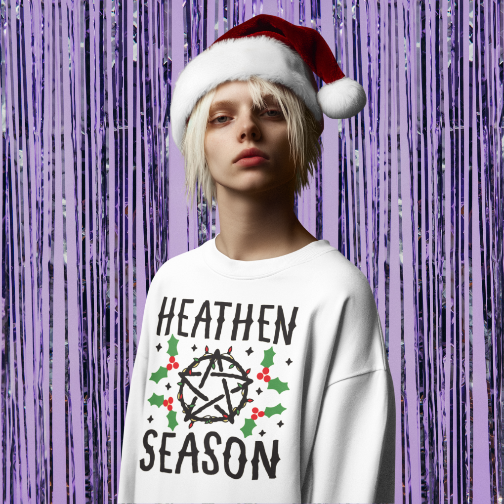 Person wearing a white sweatshirt with 'Heathen Season' text and a Santa hat against a purple curtain background