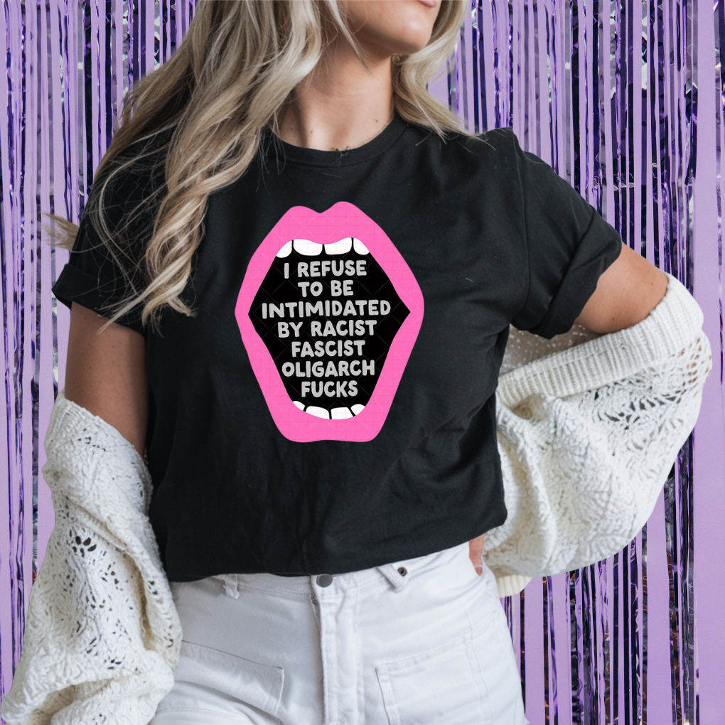 Person wearing a black t-shirt with a graphic design and text, standing against a purple curtain background.