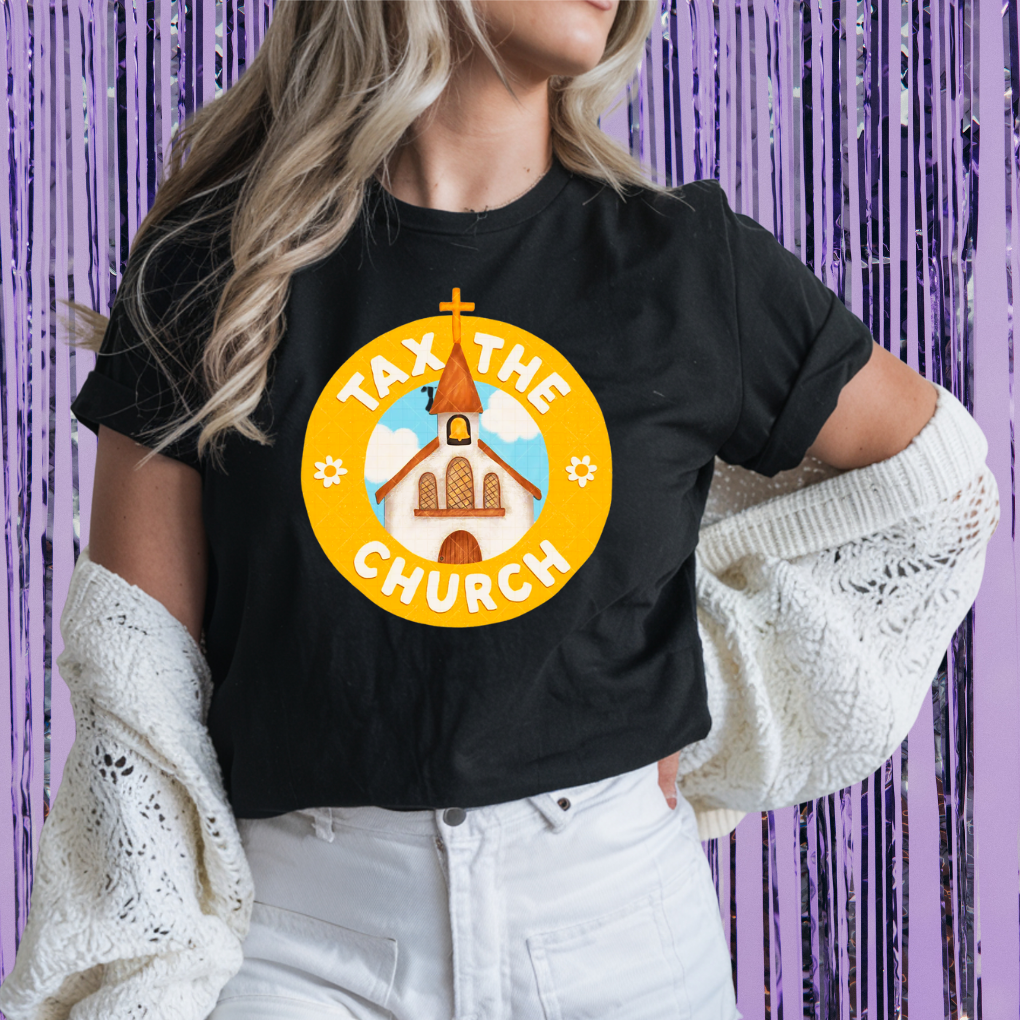 Person wearing a black t-shirt with 'Tax the Church' graphic design against a purple curtain background